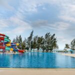 A photo of a colourful water slide next to a clear swimming pool surrounded by greenery.