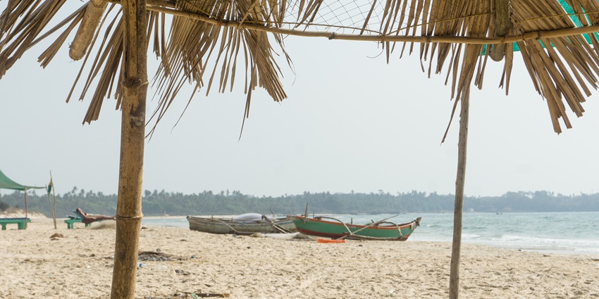 Sandy beach with fishing boats and a thatched shade hut, overlooking calm blue sea waters.