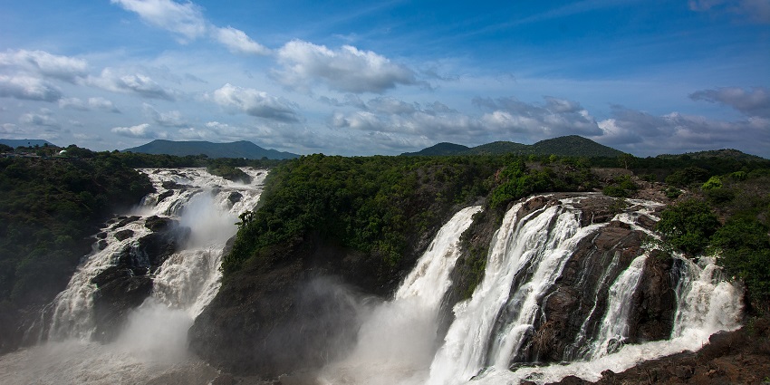 Shivanasamudra Falls cascade over rocks surrounded by green vegetation under a blue sky