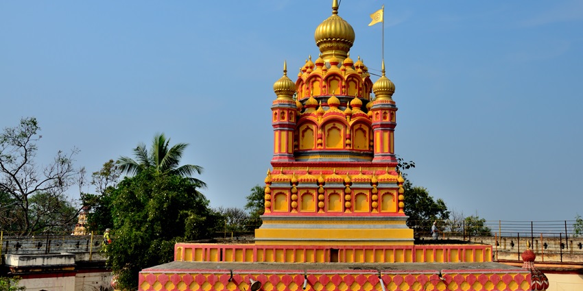 A picture of the majestic gopuram of a temple with intricate architecture and a flag on top