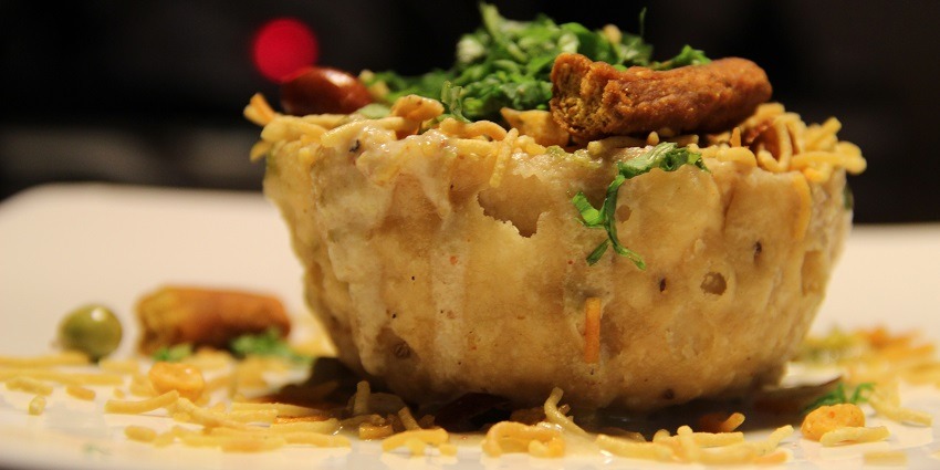 Katori Chaat topped with sev, peanuts, peas and coriander leaves served on a white plate.