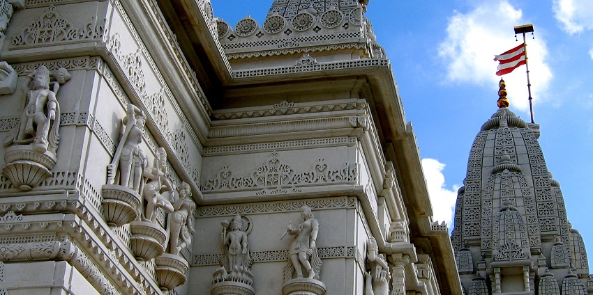 Marble temple adorned with detailed carvings and saffron-striped flags fluttering atop.