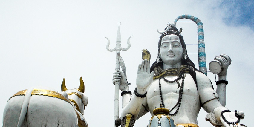 A giant statue of Lord Shiva is placed on the roof of a temple behind its main entrance.