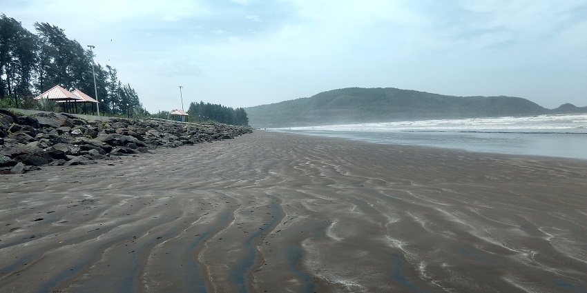 A wide, sandy beach stretches towards the ocean under a cloudy sky, with a rocky shoreline