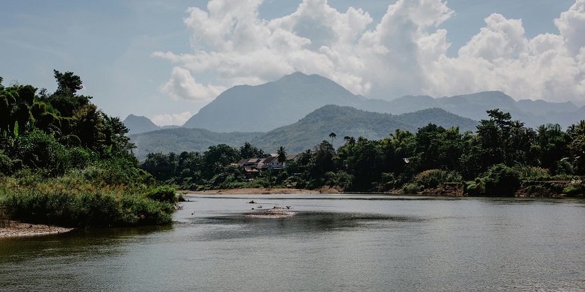 A picture of the bank of a river in a lush green valley with a hill in the backdrop.