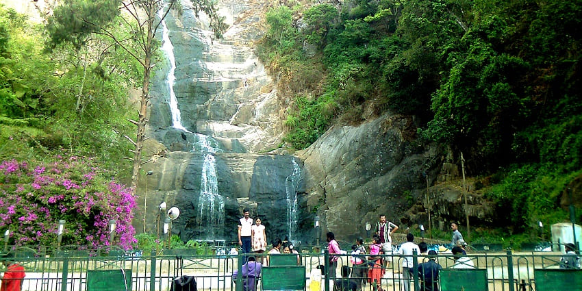 Waterfall spilling over rocks into a pool, framed by lush vegetation for travellers.