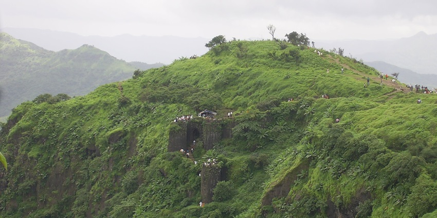 Slopes of Sinhagad Fort with ancient stone walls and green valleys crowded with tourists for Paragliding near Pune.