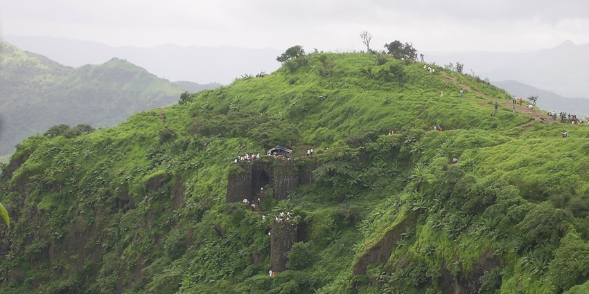 Sinhagad Fort in Maharashtra stands tall against a clear blue sky, surrounded by hills.