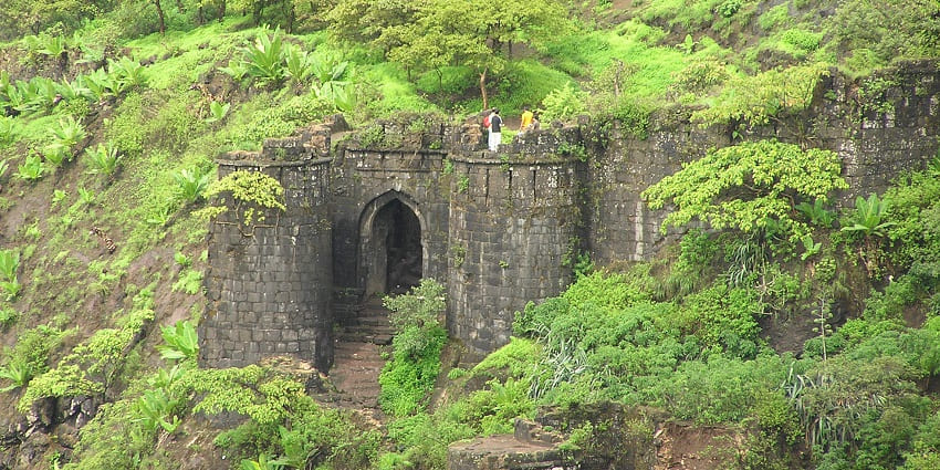 Image of Kalyan Darawaja on Sinhgad Fort surrounded by lush greenery and people trekking on top of the hill
