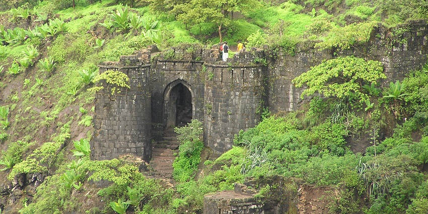 A panoramic view of Sinhagad Fort, atop a hill, surrounded by lush valleys and nature.