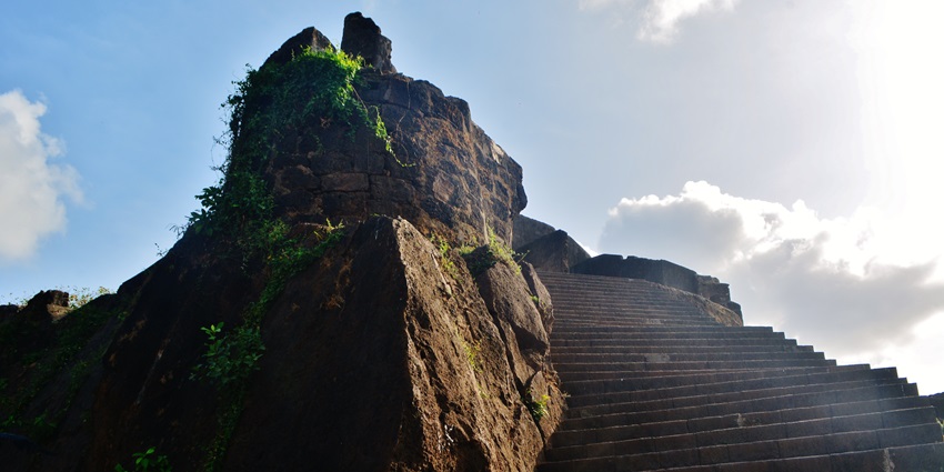 Stone steps leading up historic Sion fort with large rocks and green vines under blue sky.