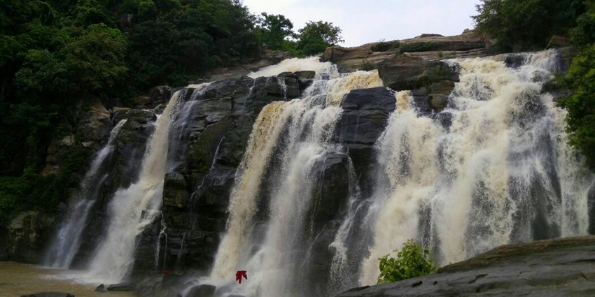A picture of a waterfall in Jharkhand with water cascading down a rocky hill surrounded by greenery