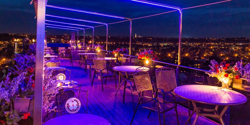 Image of a roof top cafe with vibrant lights flower decorated seating area and stunning city view