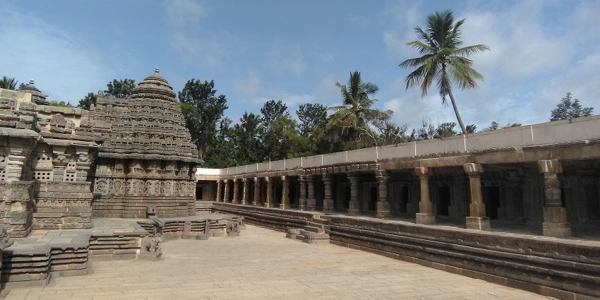 Chennakesava Temple with intricate carvings, pillars, and palm trees under cloudy sky