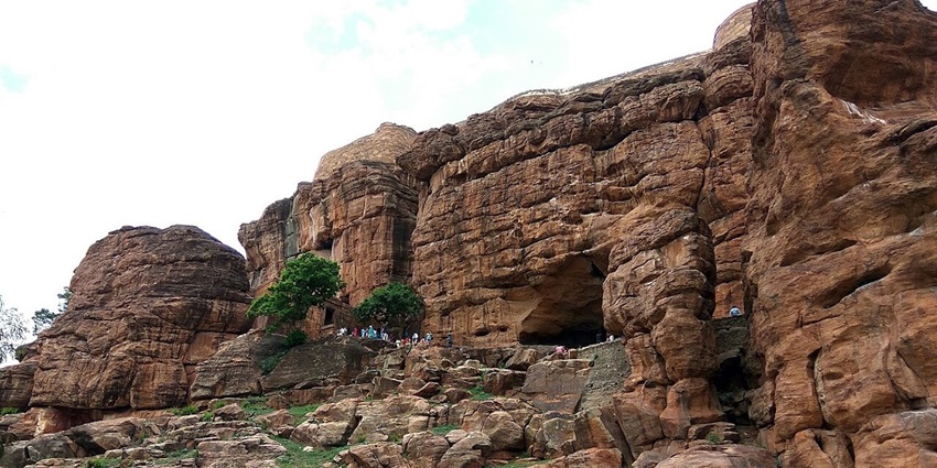 Ancient rock-cut temple with intricate bas-relief sculptures of Shiva, Vishnu, and Brahma.