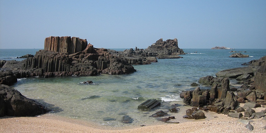 St. Mary's Island in Udupi with clear water, sandy shore, and large rock formations.