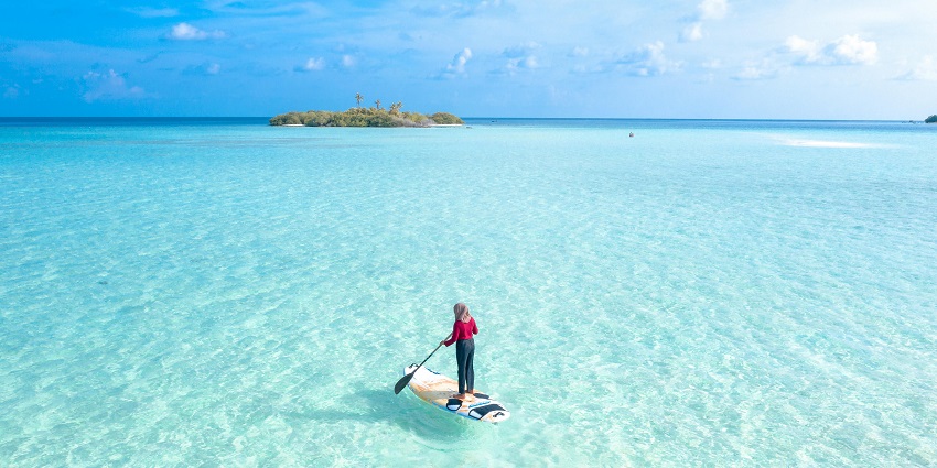 An image of a person standing on a paddleboard, gliding across calm waters, surrounded by nature.