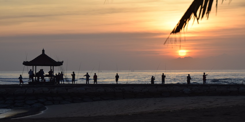 Fishermen gather at the Nusa Dua Beach in Bali, a scenic sunrise in the background.