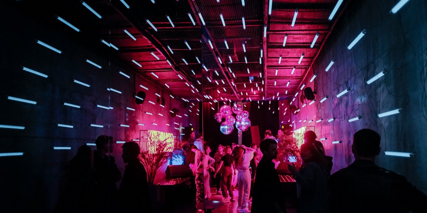 Image of a club in blue and pink vibrant colours light and people enjoying their drinks and dancing