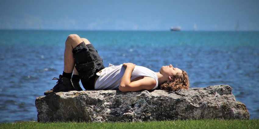 An image of a person relaxing on a lounge chair under a sun umbrella near the shore in Dreamland Beach.