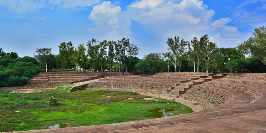 A picture of the dried-up Surajkund reservoir with trees and greenery in the background