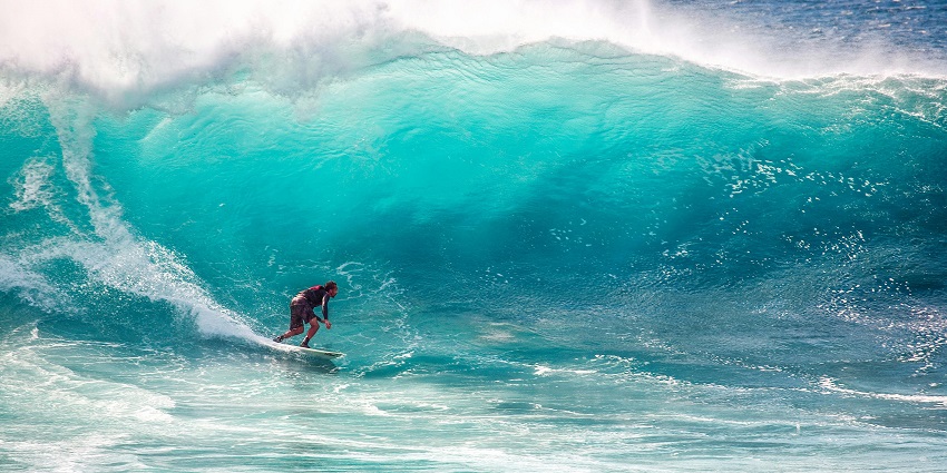 An image of a surfer catching a wave at Balangan Beach with cliffs in the background.