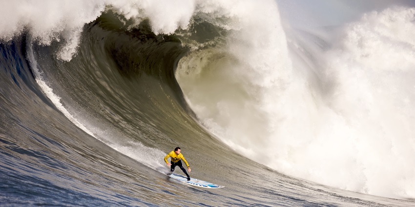 A picture of a man surfing at a beach in Dapoli with a massive wave behind him
