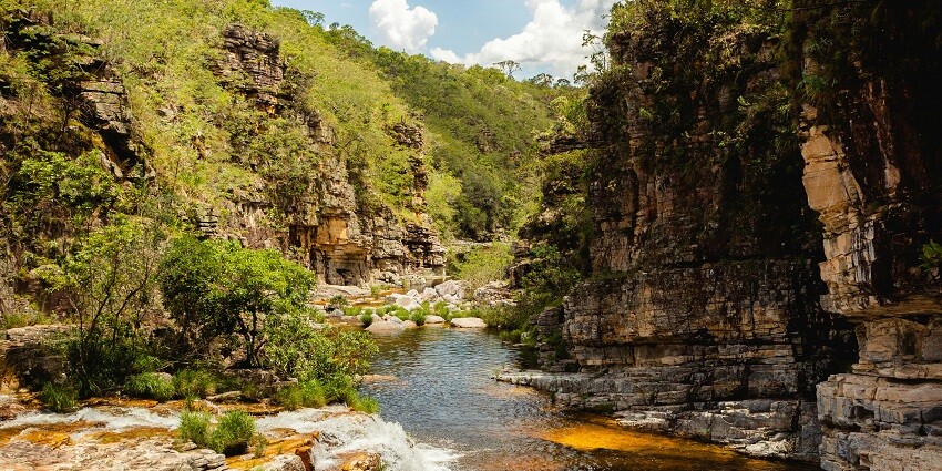An image of a waterfall flowing between rocky banks where one can even swim.