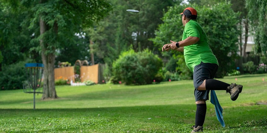 A person throwing a disc towards a grassy park with trees in the background
