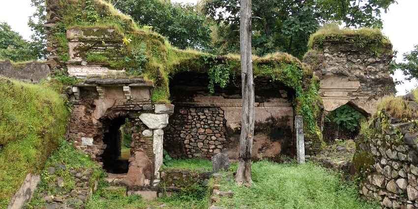 Front view of the ruins of Raja Ki Baithak in Deogarh Fort with cattle grazing the fields