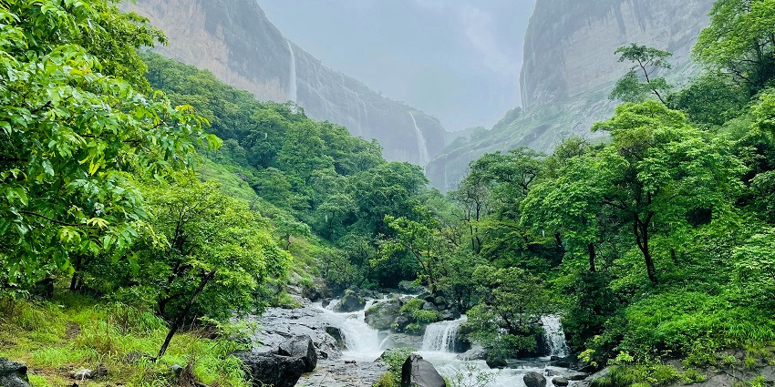 The misty slopes of Tamhini Ghats covered in greenery and waterfall under a cloudy sky.