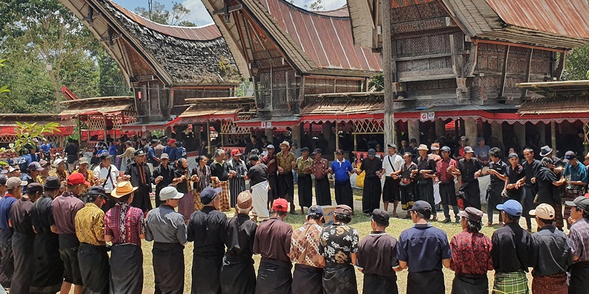 A funeral ceremony with locals in front of boat-shaded arched houses in Tana Toraja