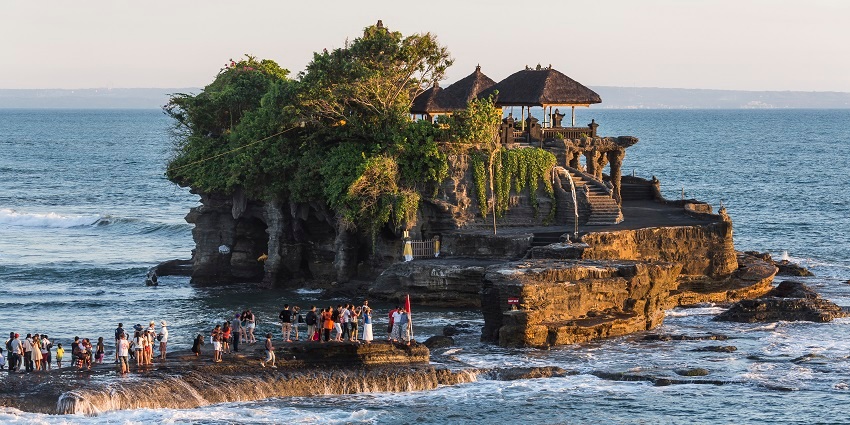 Sunset view of Tanah Lot temple on a rock formation in the middle of Ocean, one of the famous places to visit in Bali.