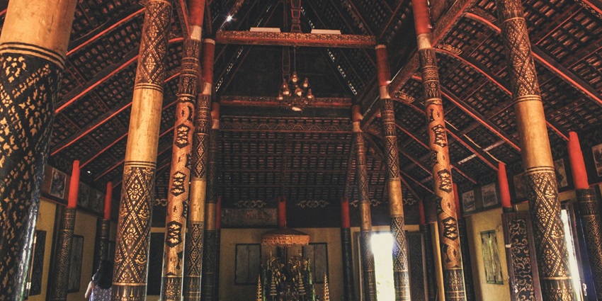 Traditional interior with intricately carved pillars and a high, thatched roof ceiling