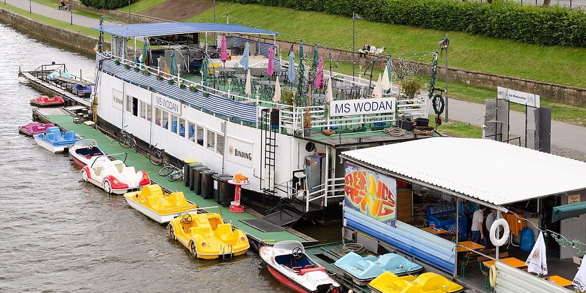 Photo of a floating restaurant with an upper deck, and chairs anchored to the shore.