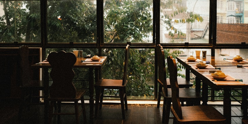 Restaurant interior with tables and chairs beside large windows overlooking cityscape