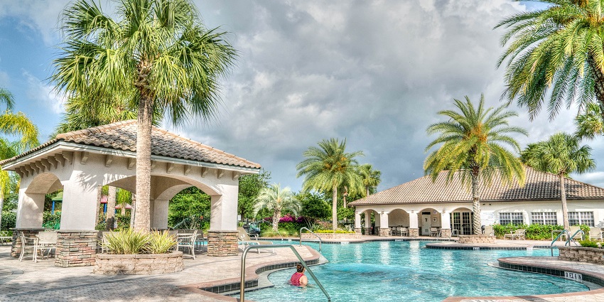 A group of people relaxes by a tropical pool, enjoying the sunny weather and blue water.