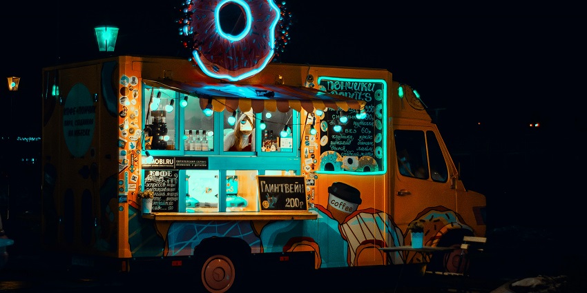 An orange-coloured food truck featuring serving windows and a menu board with an LED logo