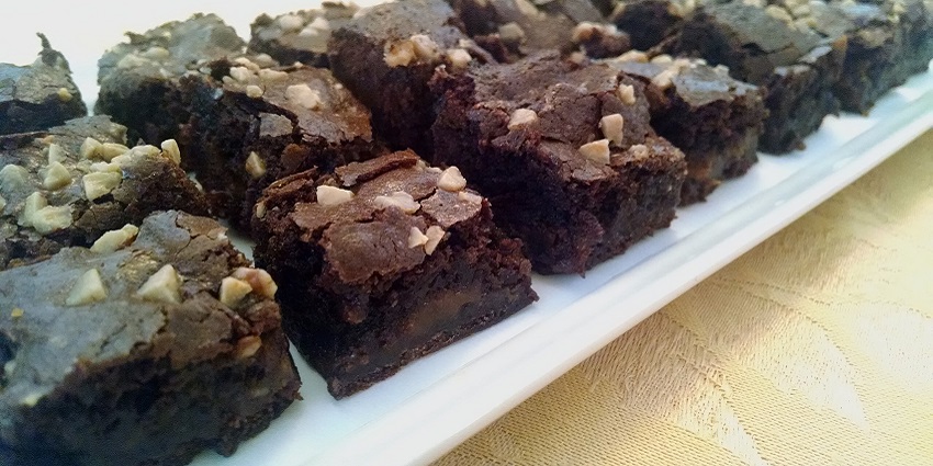 Pieces of Salted Caramel Brownies topped with cut nuts, served on a plate in a restaurant.
