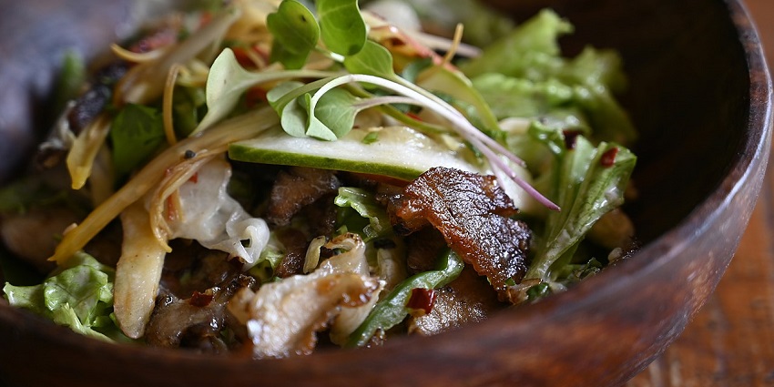 Char-Siu Pork Salad, an Oriental dish served in a wooden bowl topped with cucumber and herbs.