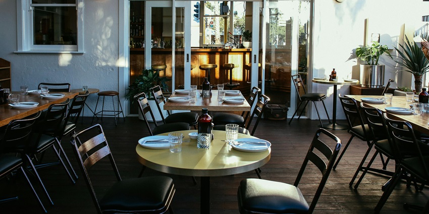 Rustic restaurant terrace with wooden tables and chairs amid lush greenery.