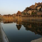 The image shows stone ruins and a large temple complex in Hampi, Karnataka, surrounded by rocky hills.