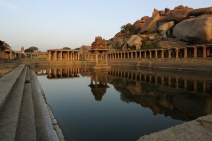 The image shows stone ruins and a large temple complex in Hampi, Karnataka, surrounded by rocky hills.