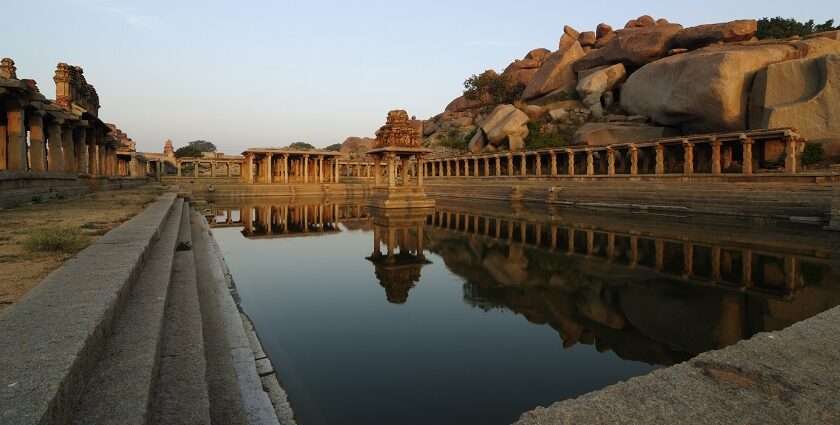 The image shows stone ruins and a large temple complex in Hampi, Karnataka, surrounded by rocky hills.