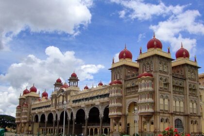 Mysore Palace in the morning, with golden domes and arches, surrounded by greenery and clear skies.