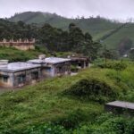 An image of a scenic Megamalai, featuring lush green mountains and quaint houses.