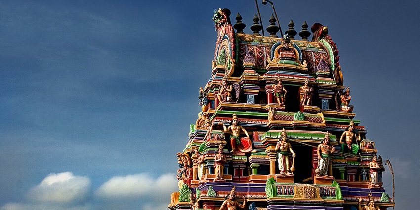 An image showing a Gopuram of Thiruneermalai Temple with intricate carvings and a bright blue sky