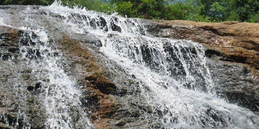 A seasonal waterfall with two distinct streams, surrounded by lush greenery and trekking trails.