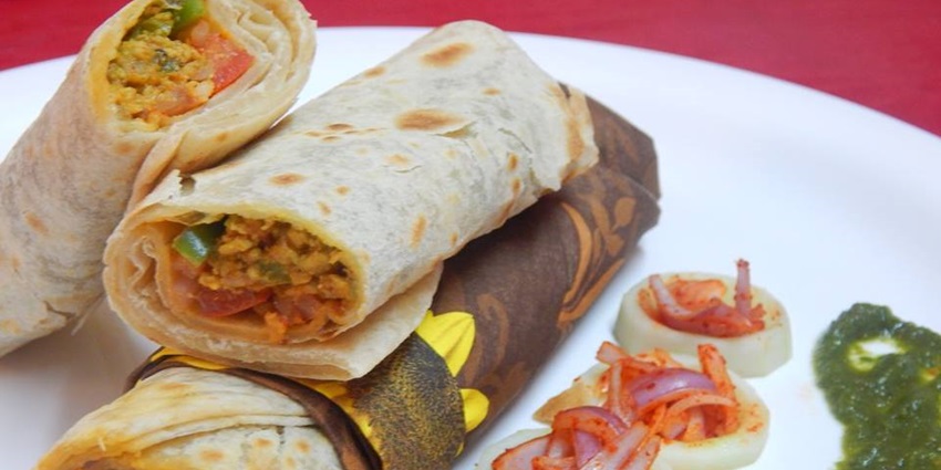 One vegetable frankie cut into halves and the other one whole are served with sauces.