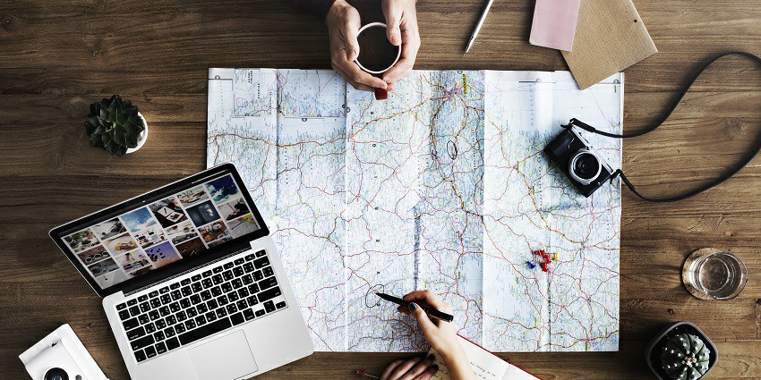 A laptop, camera, notebook, a coffee cup kept on a displayed map over a table.